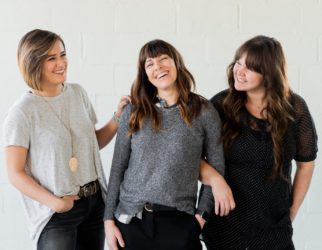 3 women smiling and standing beside white wall