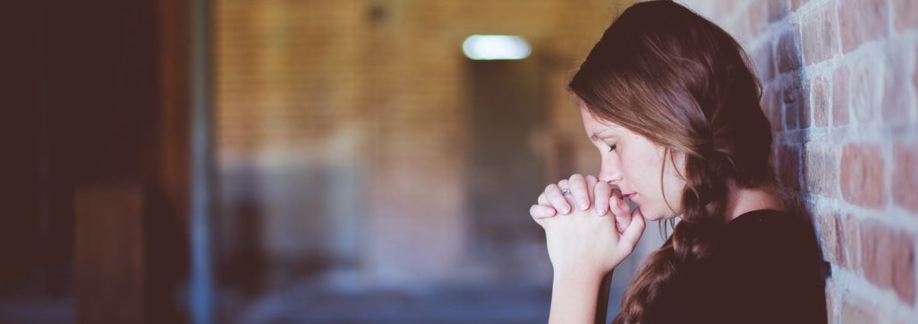 woman praying while leaning against brick wall