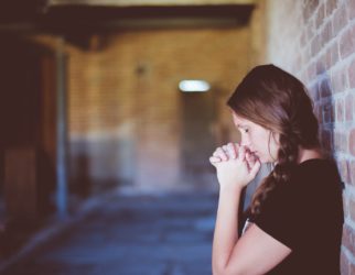 woman praying while leaning against brick wall